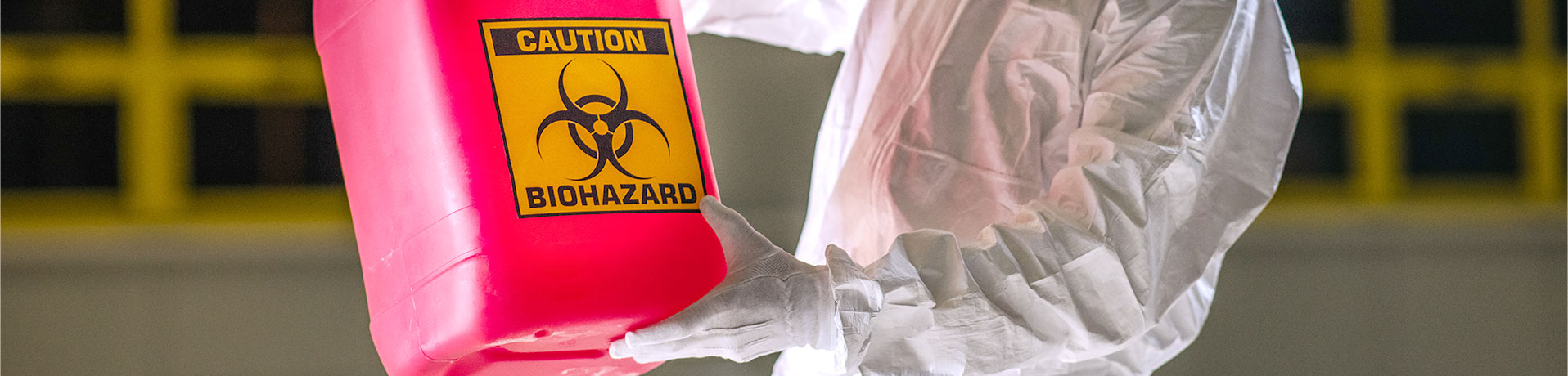 Cleaning person in full personal protective equipment holding a container especially meant for biohazard waste