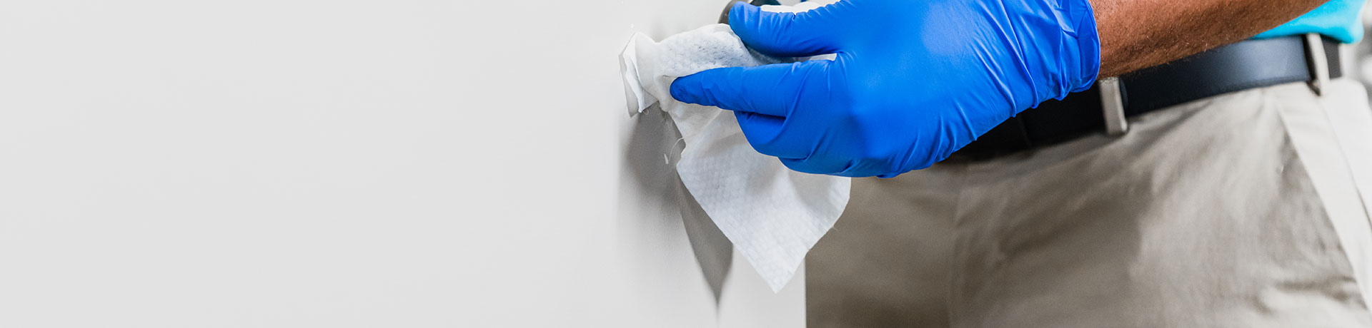 Cleaning person wearing protective latex gloves using a disinfection wipe on a door handle