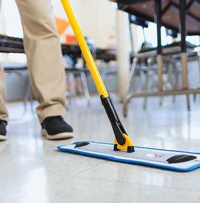 Cleaning person using a microfiber mop to wipe dust and debris off industrial laminate flooring 