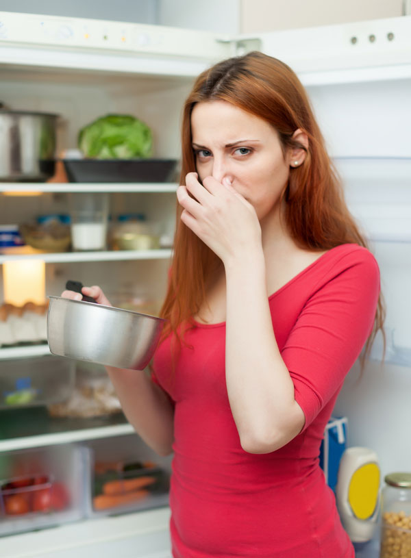 Woman holding her nose in front of a refrigerator