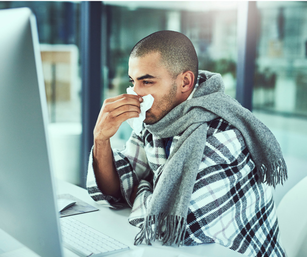 Guy sitting at computer in office blowing his nose
