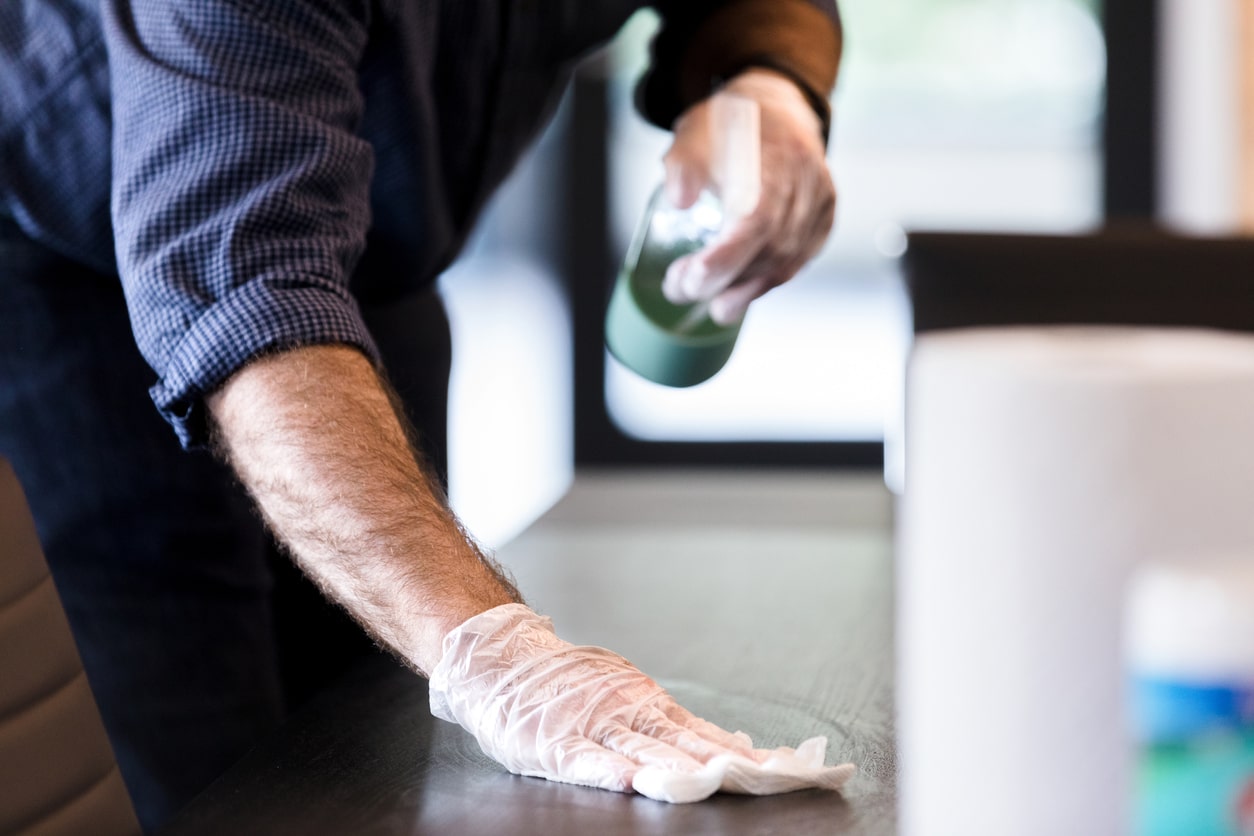 A business owner disinfecting an office table with disinfecting solution and paper towels.